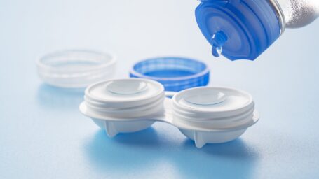 Case of contact lenses placed on a blue background. Pouring the protective solution.